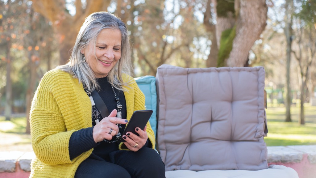 An elderly woman on her phone in an outdoor setting with trees behind her